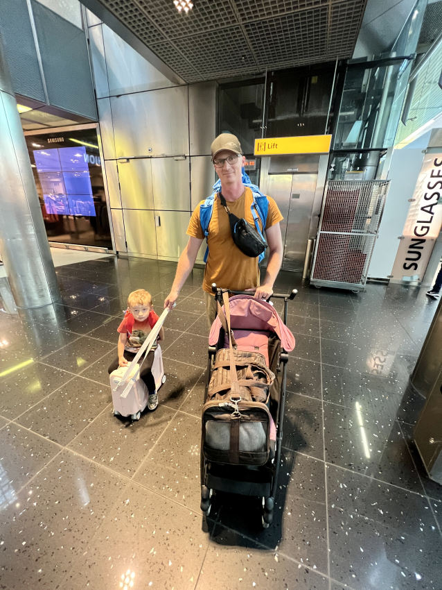 Father navigating the airport with ease, his child riding along on a Jetkids tokke ride-on suitcase, simplifying family travel.