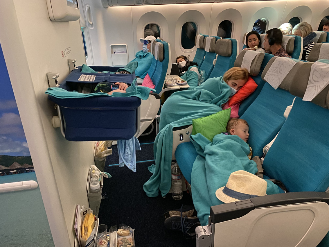 Family sleeping comfortably on a long-haul flight with airplane bassinets in use for the infant