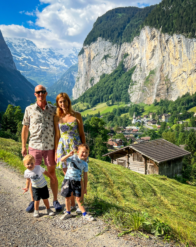 Family posing against the backdrop of a lush green valley in Switzerland, creating memories with kids on a scenic hike.