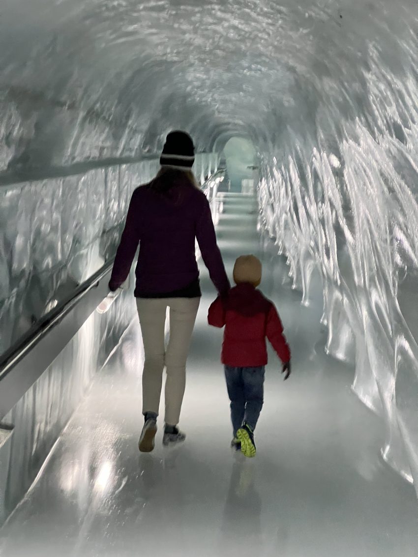 Mother and child walking hand in hand through a glittering ice tunnel, exploring the magical frosty wonders of Switzerland with kids.