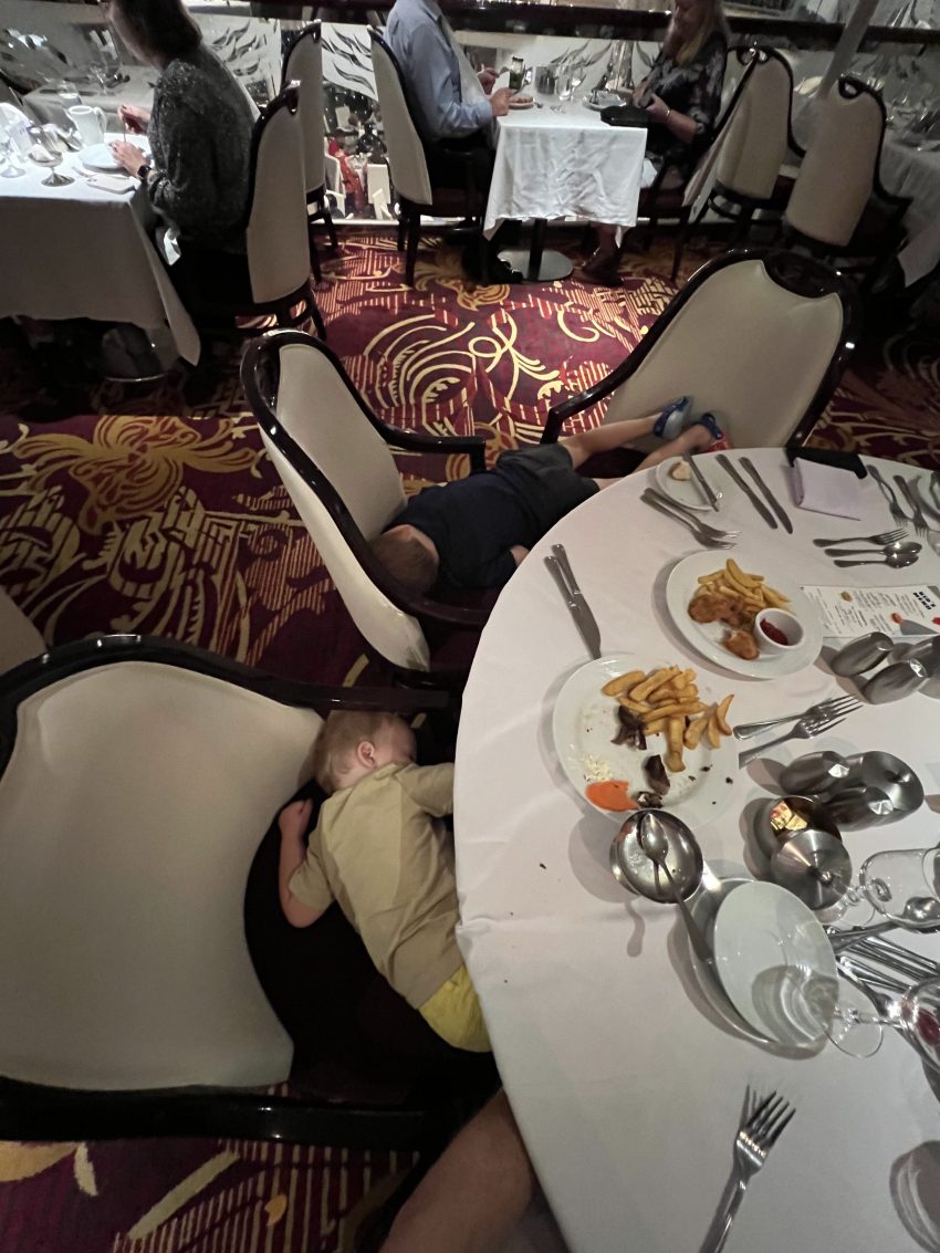 Exhausted child asleep under a table after a meal, a real moment when cruising with a toddler.